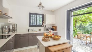Een moderne keuken met een groot raam, een eethoek met een tafel en stoelen, en uitzicht op een tuin.