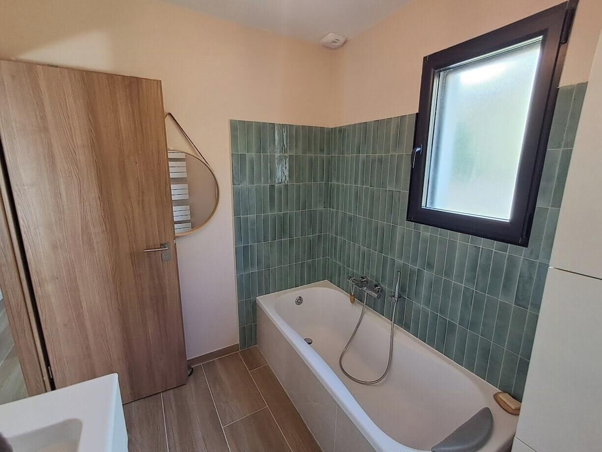 A bathroom with a bathtub, a wooden wardrobe, and a window.