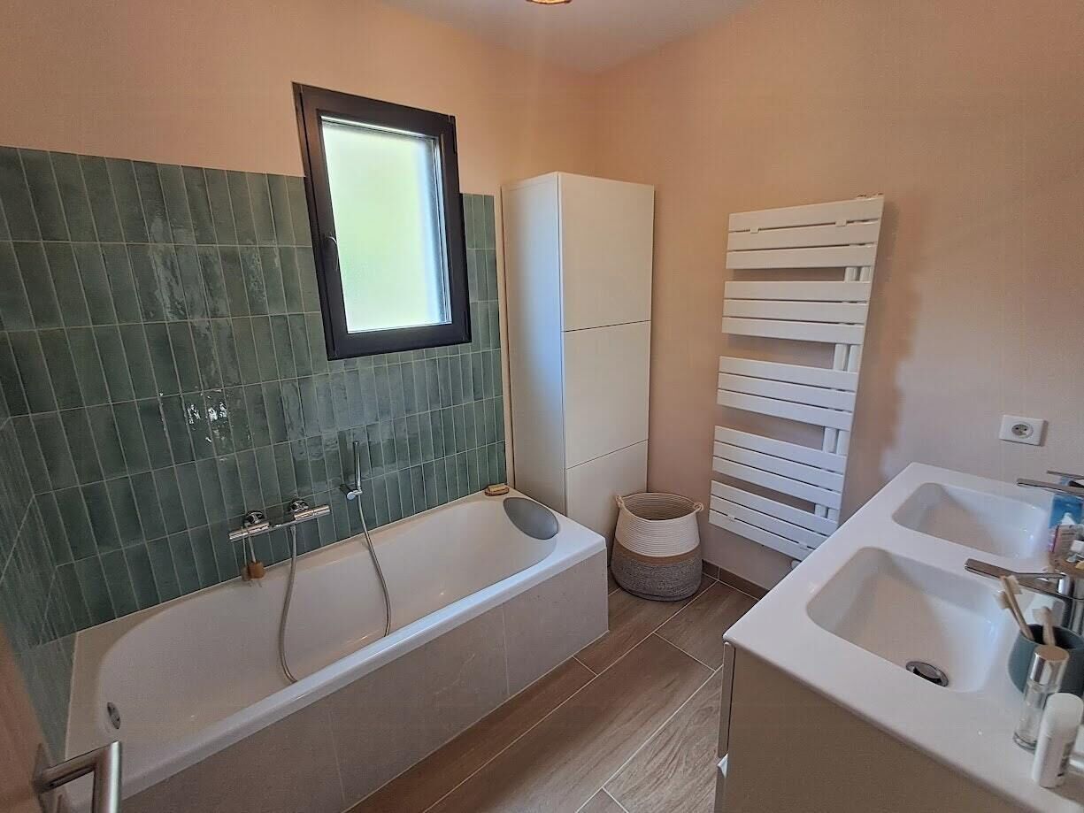 A bathroom with a bathtub, a sink, a window, and a towel rack.
