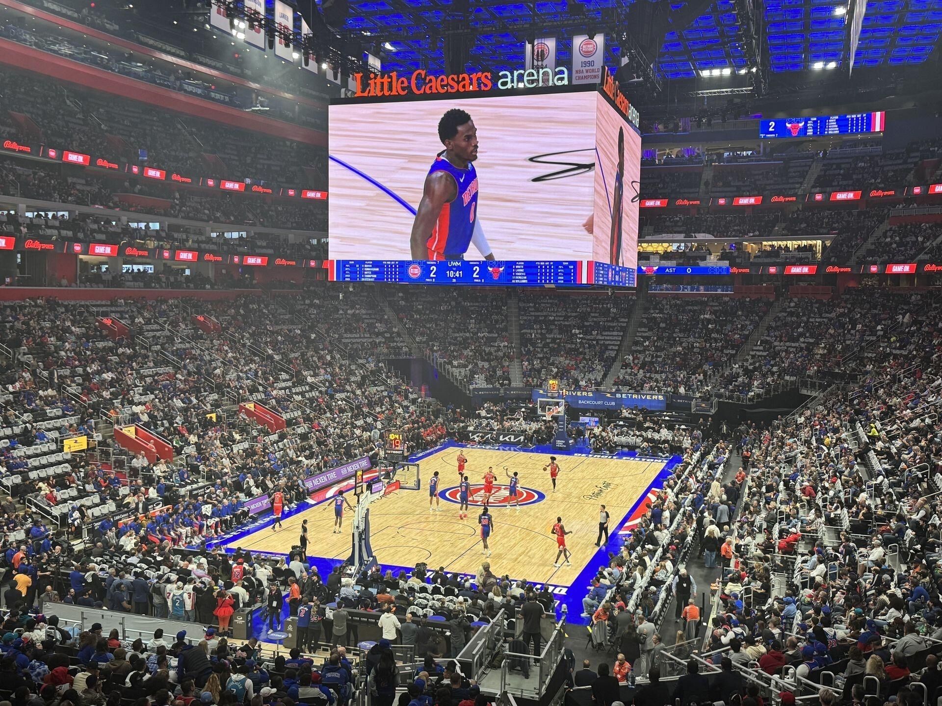 A basketball game at the Little Caesars Arena with a large crowd.