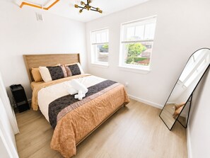 Ein Schlafzimmer mit einem Bett, einem Nachttisch, einem Spiegel und Fenstern.