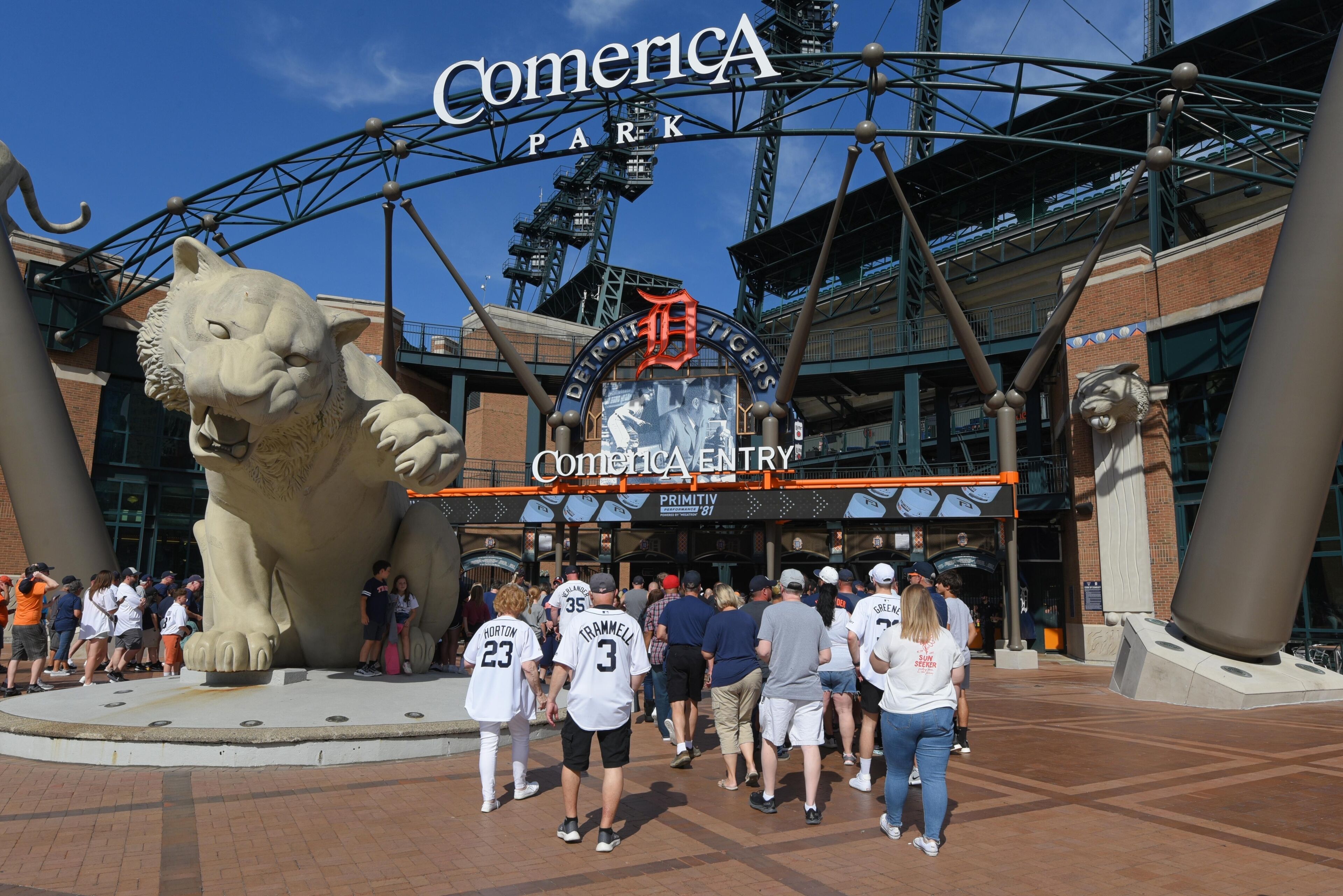 A stadium entrance with a large lion statue, a sign for Comerica Park, and people entering.