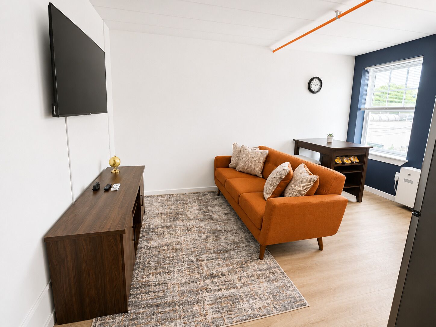 A modern living room with a sofa, a TV mounted on the wall, a small table, and a clock on the wall.