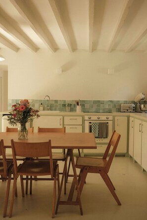 Una cocina con una mesa de comedor, sillas, un florero con flores, un lavamanos, una estufa y un tostador.