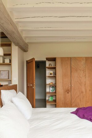 Un dormitorio con una cama, un armario de madera, una estantería con objetos y una puerta que da a otra habitación.