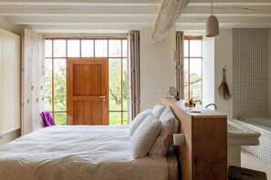 Ein Schlafzimmer mit Holzkopfstütze, einem Bett, einem Fenster und einem Badezimmer mit Waschbecken und Spiegel.