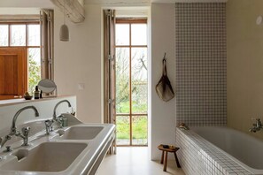 Un baño con bañera, lavamanos y ventana con vistas a zonas verdes.