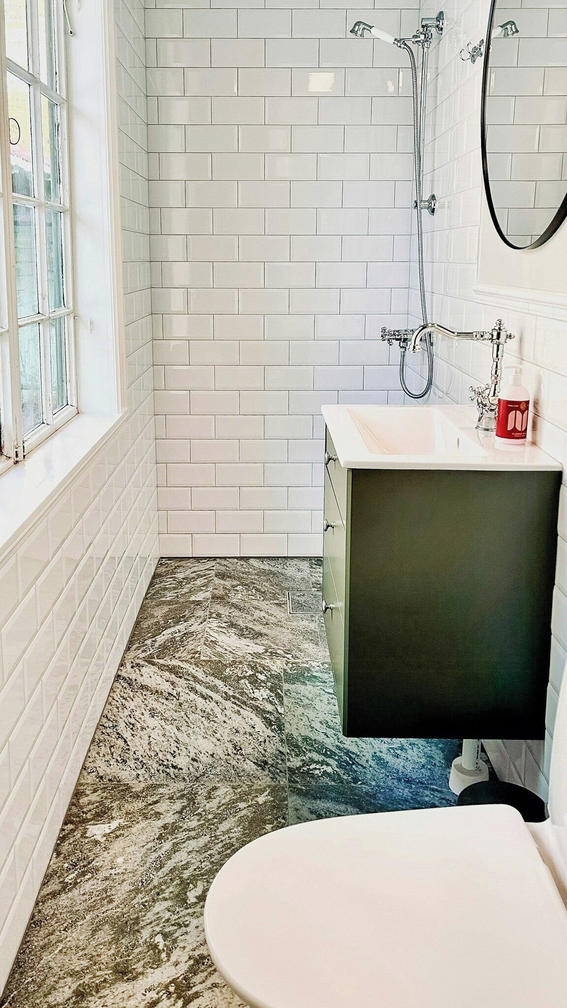 Een badkamer met witte betegelde wanden, een douche, een wastafel en een toilet.