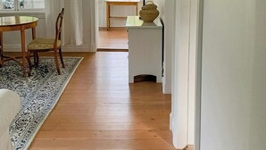 Ein Zimmer mit Holzboden, einem Esstisch mit Stühlen, einer Lampe und einem kleinen Tisch mit einer Dekoration.