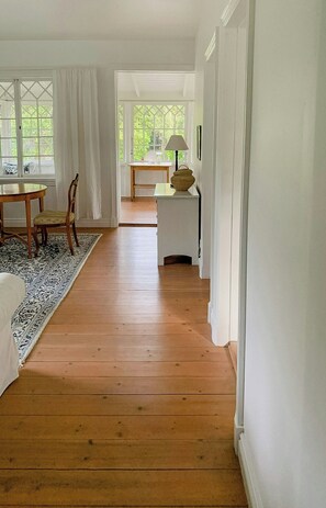 Une pièce avec un plancher en bois, une table à manger avec des chaises, une lampe et une petite table sur laquelle est posé un objet décoratif.