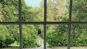 Ein Fenster mit Blick auf einen Kiesweg, der zu einer Holzterrasse führt, ein Glas mit einer Kerze und eine kleine weiße Kerze auf einer Holztischplatte.