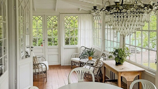 Ein Zimmer mit Esstisch, Stühlen, einer Deckenleuchte und großen Fenstern.