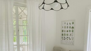 Ein Schlafzimmer mit einem großen Bett, einem Fenster mit Vorhängen, einer Wandleuchte und einem gerahmten Pflanzenbild.