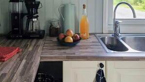 A kitchen with a coffee maker, a pitcher, a bottle of orange juice, and a bowl of apples. - Charming seaside cabin in Tingvoll (Tingvoll)