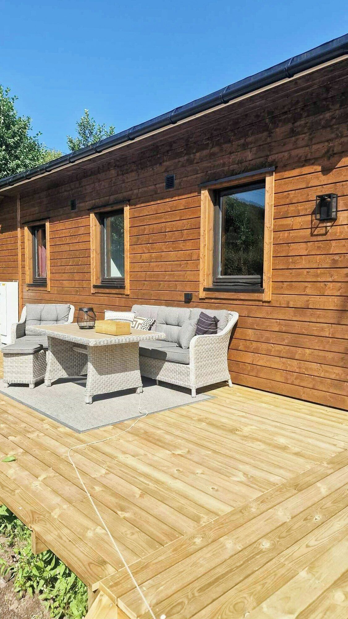 A wooden cabin with a deck, outdoor seating, and large windows.