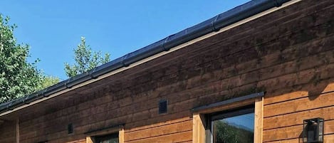 Una cabaña de madera con terraza, mobiliario exterior y ventanas grandes.