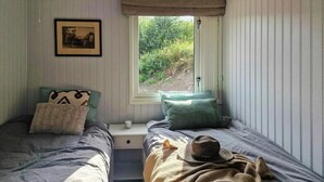 A bedroom with two beds, a window with a view of greenery, a framed picture on the wall, and a small bedside table. - Charming seaside cabin in Tingvoll (Tingvoll)