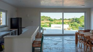 Una cucina moderna con un'ampia finestra, un'area pranzo con sedie di legno e vista su un paesaggio verde.
