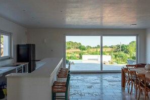Une cuisine moderne dotée d’une grande fenêtre, un coin repas avec des chaises en bois et une vue sur un paysage verdoyant.