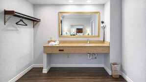 A bathroom with a wooden floor, a granite countertop sink, a gold-framed mirror, a towel rack, and a trash bin.