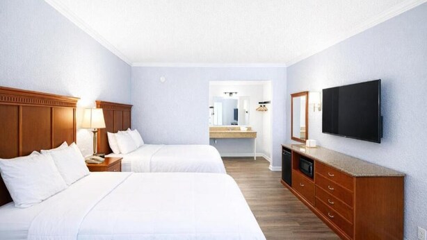 A hotel room with two beds, a wooden dresser, a television, and a bathroom visible through an open door.