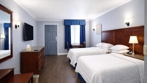 A hotel room with two beds, a desk, a dresser, a TV, and a door.