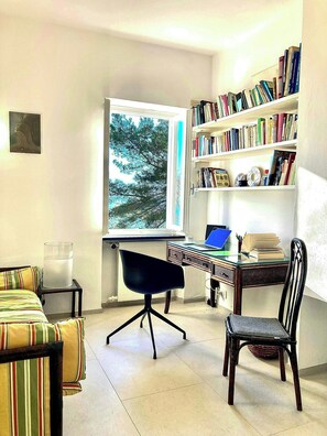 Une pièce comprenant un bureau, une chaise, une bibliothèque et une fenêtre donnant sur des arbres.
