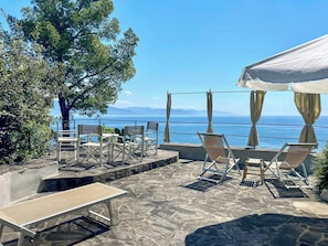 An outdoor seating area with chairs and a table, overlooking a body of water and mountains.