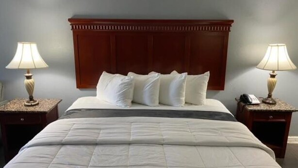 A neatly made bed with a wooden headboard, two bedside lamps, and a telephone on the nightstand. - KS-King Smoking, Comfort Room, One king Bed, (Antioch)