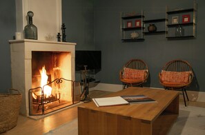 Ein Wohnzimmer mit Kamin, zwei Korbstühle, einem Holztisch und Wandregalen mit Dekoration.