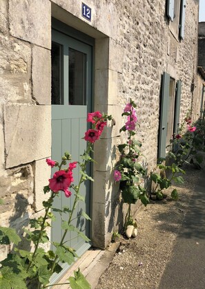 Ein Steingebäude mit der Hausnummer 12, einer Tür und rosa Blumen an der Seite.
