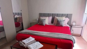 A bedroom with a bed, bedside tables, a mirror, and a small table with towels.