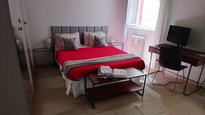 A bedroom with a bed, a desk, a chair, a radiator, and a window.