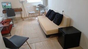 A living room with a sofa, a small table, a chair, a TV, and a radiator.