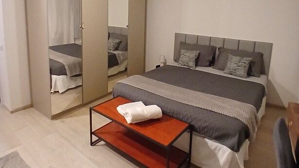 A bedroom with a bed, a mirror, a wardrobe, and a small table.