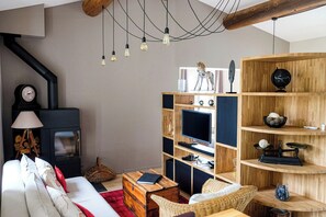 Ein Wohnzimmer mit einer Couch, einem Couchtisch, einem Fernseher, einem Bücherregal, einem Kamin und einer Pendelleuchte.