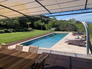 Ein Schwimmbecken mit einer Pergola darüber, umgeben von einer Holzterrasse und Liegestühlen.