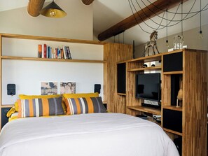 Ein Schlafzimmer mit einem Bett, Holzregalen, einem Fernseher und einer Pendelleuchte.