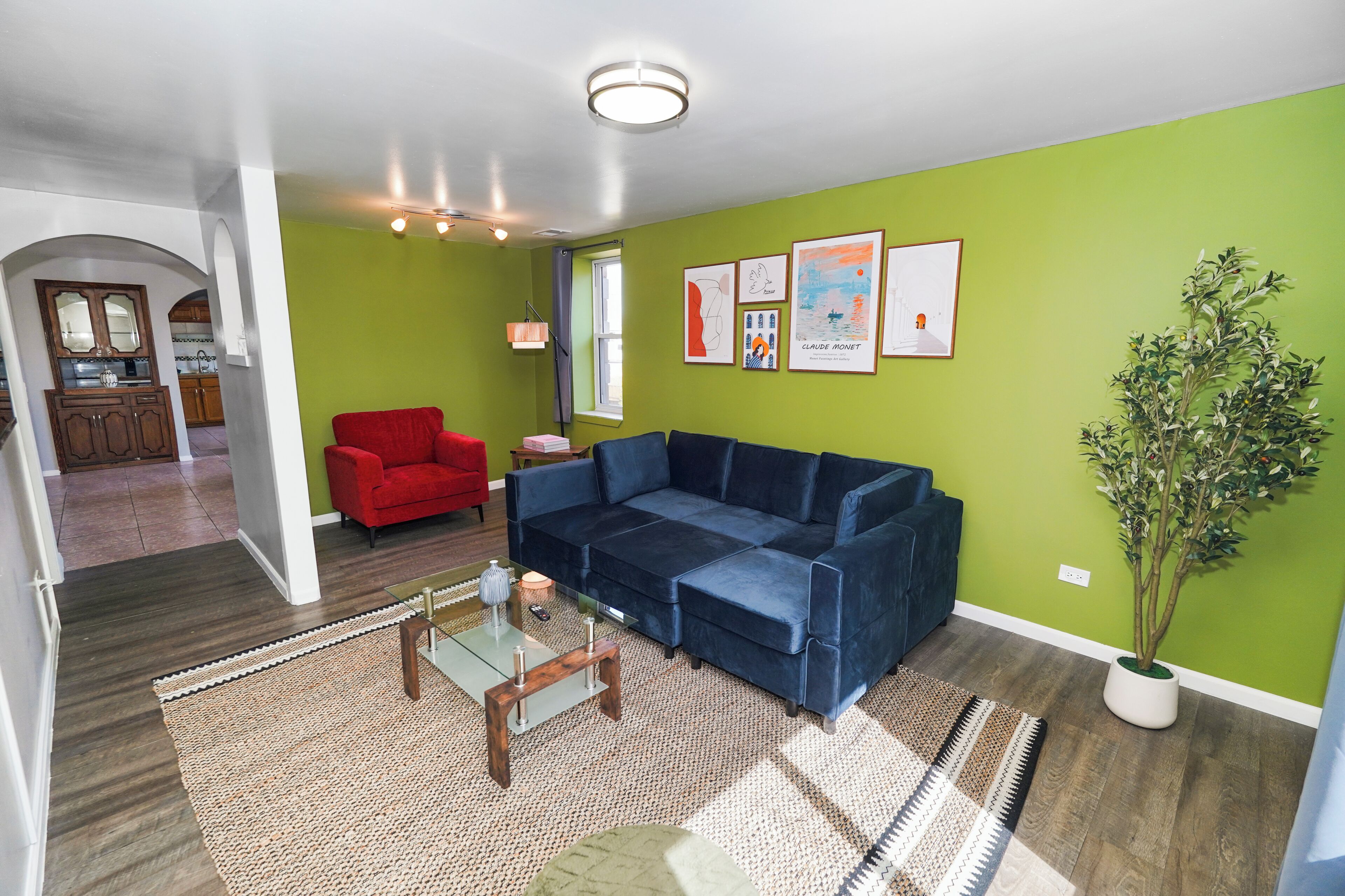 A living room with a blue sofa, a red armchair, a glass coffee table, and a potted plant.