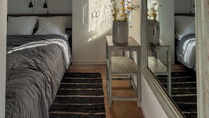 Quarto com cama, uma mesinha com planta em vaso, espelho e janela com vista.