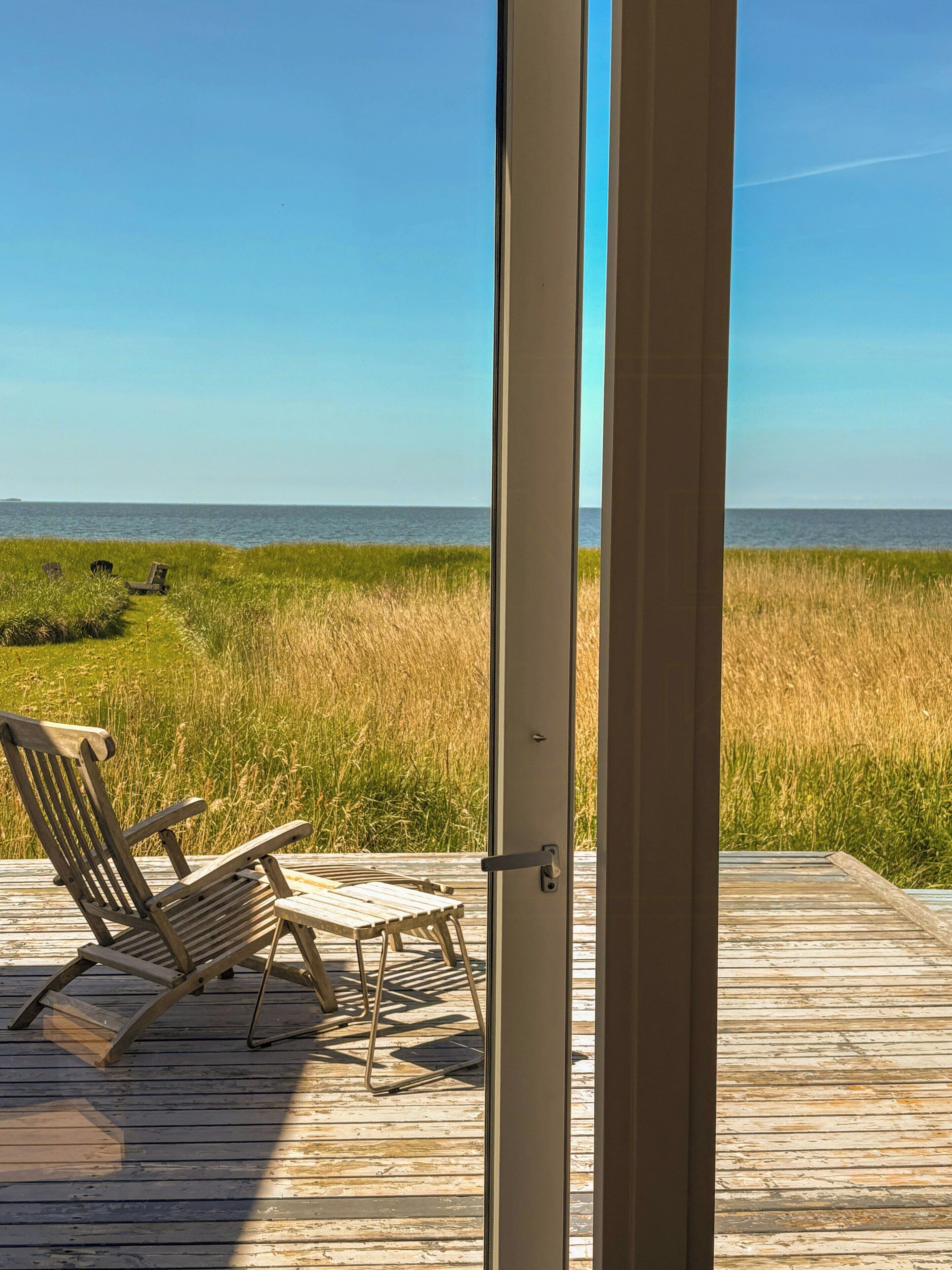 An open door leading to a deck with a view of the ocean and grassy area.
