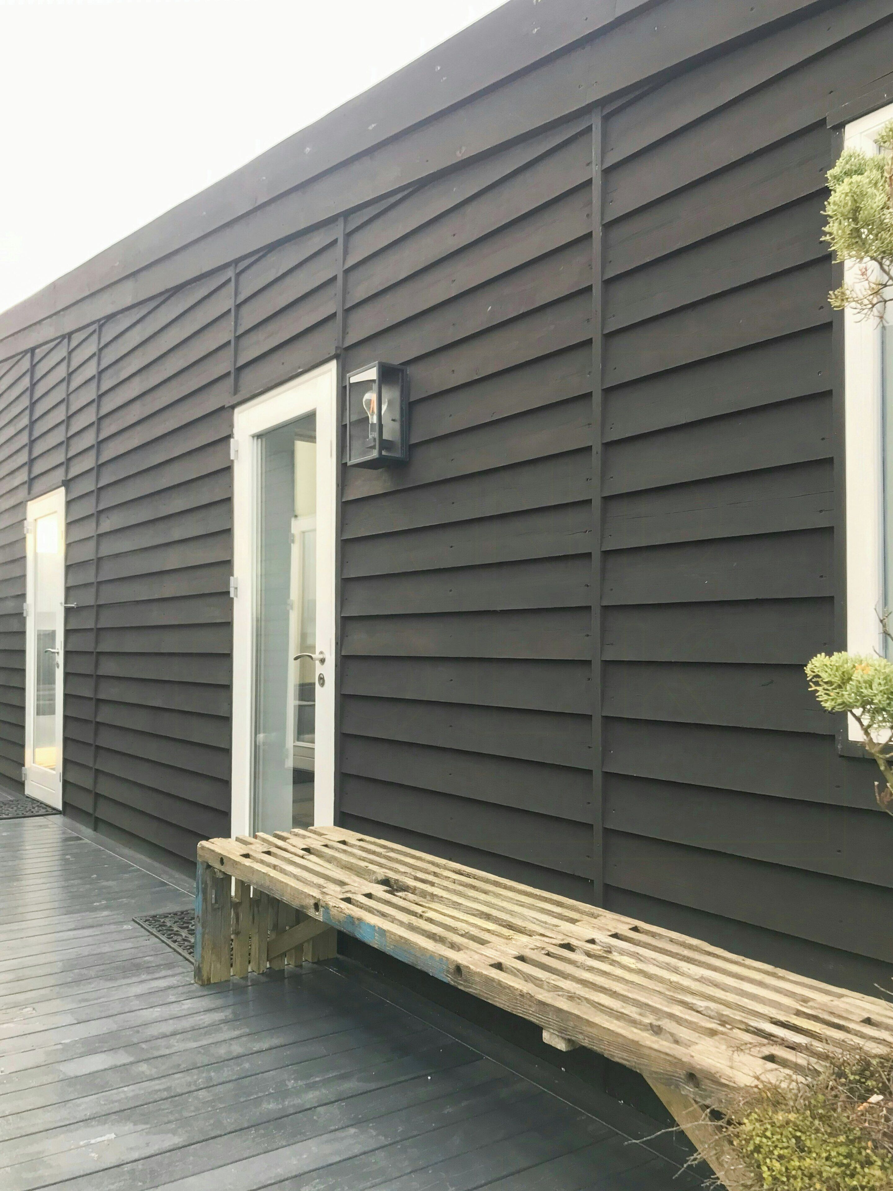 A building with dark siding, a bench, and a door.