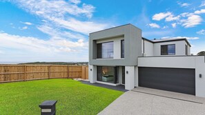 Ein modernes, zweistöckiges Haus mit Garage und einem eingezäunten Garten, strahlend blauer Himmel.