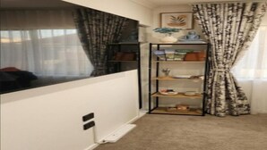 A room with a large window, a bookshelf, a carpeted floor, and a curtain. - Stylish Wesley Retreat (Auckland)