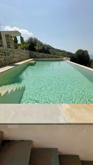 Ein rechteckiger Pool mit klarem Wasser, umgeben von einer Steinmauer und Stufen, die zum Pool hinabführen.