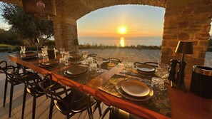 An outdoor dining area with a sunset view, stone pillars, and a long wooden table set for a meal. - Panoramic villa with pool and Capri view (Castellabate)