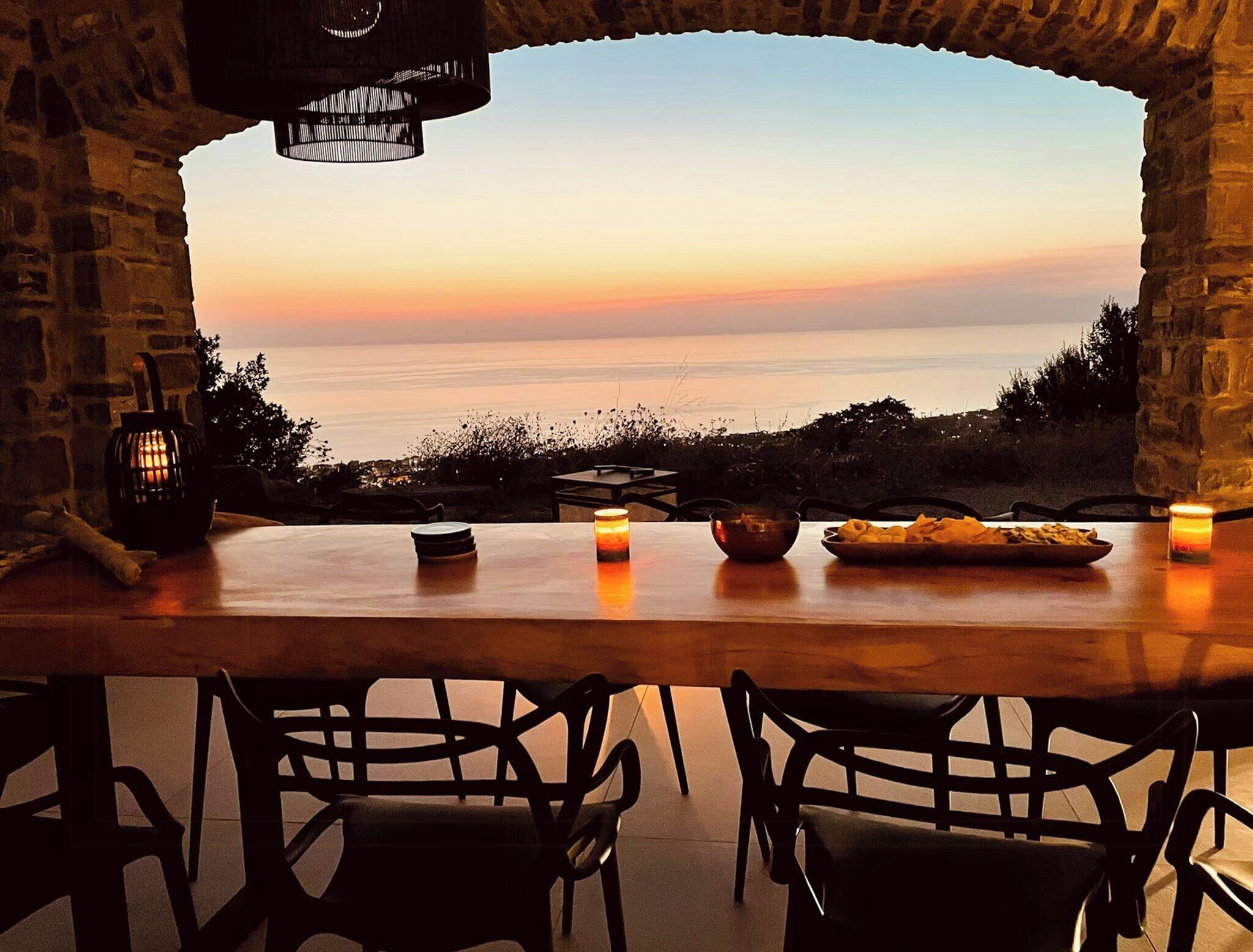 A stone-walled room with a table set for dining, overlooking a body of water.