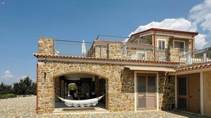 Ein Steinhaus mit Balkon, einer Hängematte und einer überdachten Sitzgelegenheit im Freien.