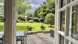 A wooden deck with a table and chairs, surrounded by a lush garden with various trees and shrubs. - Bénodet, charming stone house with beautiful garden (BENODET)