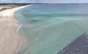 Luftaufnahme eines Strandes mit klarem Wasser, sandigem Ufer und dichter Vegetation im Hintergrund.